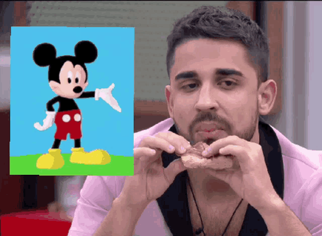 a man eating a sandwich with a picture of mickey mouse in the background