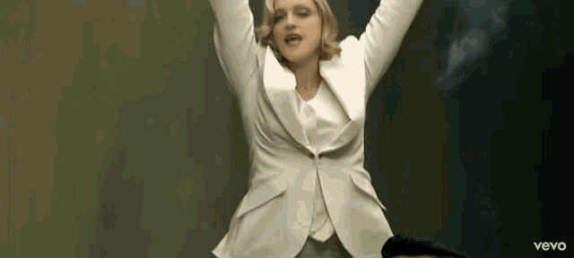 a woman in a white suit is dancing with her arms in the air and the word vevo is on the bottom