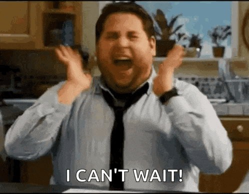 a man in a tie is making a funny face in a kitchen and saying `` i can 't wait '' .