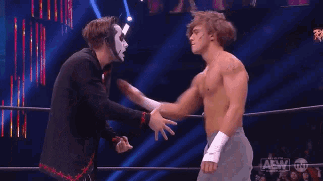 two men are wrestling in front of a crowd and one of them is wearing a mask .