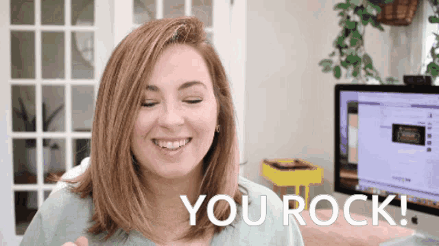 a woman smiles and says you rock in front of a computer monitor