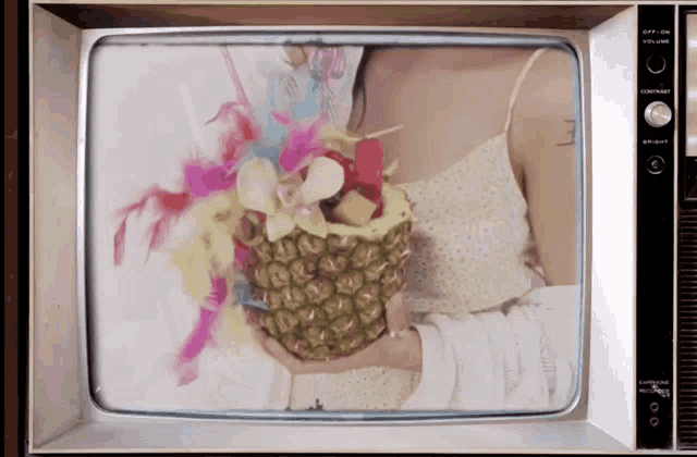 a tv screen shows a woman holding a pineapple in her hand