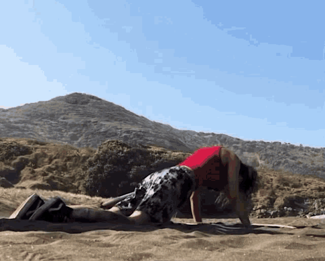a woman in a red shirt is doing push ups on a beach