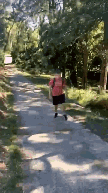a man in a red shirt and shorts is running down a path