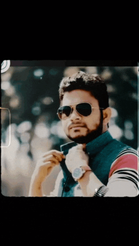 a man wearing sunglasses and a watch adjusts his shirt