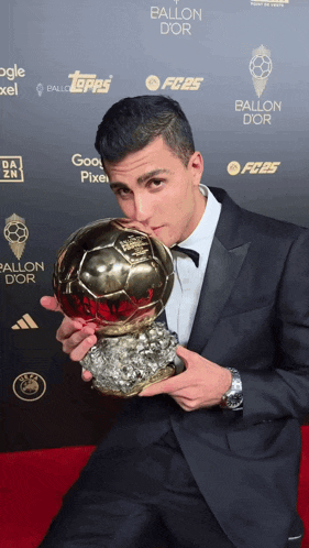 a man in a suit holds a trophy in front of a wall that says ballon dor