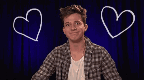 a young man is making a heart shape with his hands in front of a blue background with hearts drawn on it .