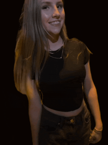a woman wearing a black crop top and jeans smiles for the camera