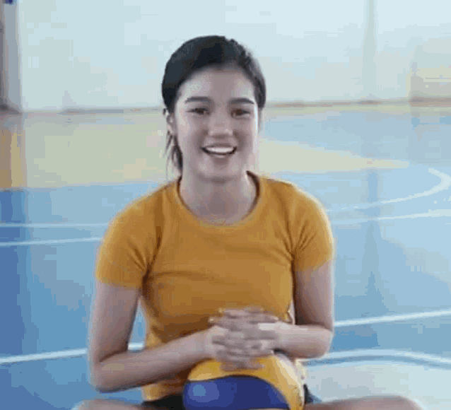 a young woman is sitting on the floor with a volleyball in her lap and smiling .
