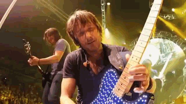 a man is playing a blue guitar on stage while another man plays a guitar