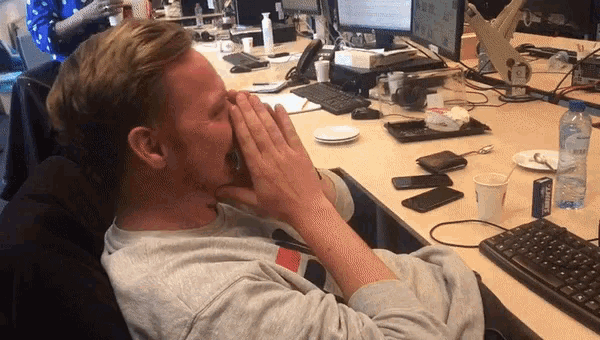 a man sitting at a desk covering his face with his hands while talking on a cell phone