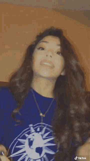 a woman with long hair is wearing a blue shirt and a gold necklace .