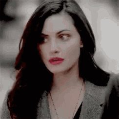 a woman with long dark hair and red lipstick is wearing a grey jacket and a necklace .