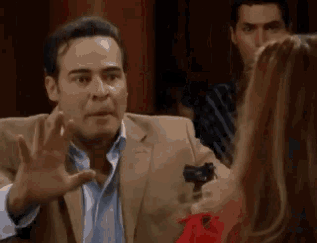 a man in a suit is pointing a gun at a woman in a red dress .