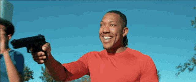 a man in a red shirt is pointing a gun at the sky