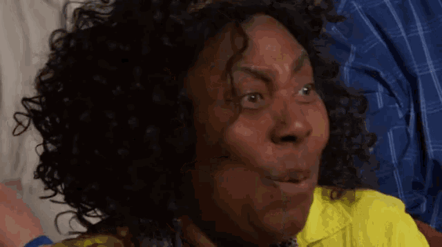 a woman with curly hair and a yellow shirt making a surprised face