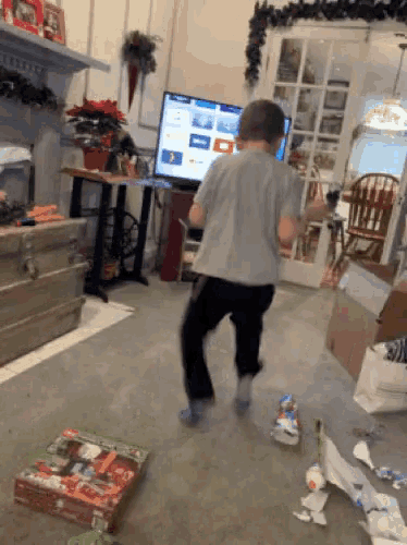a boy is dancing in a living room with a box of lego in the foreground