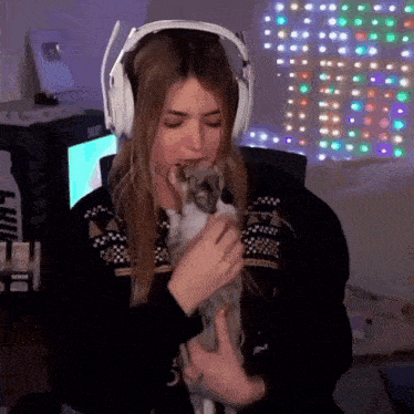a woman wearing headphones is holding a cat in her lap .