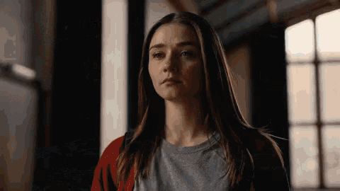 a woman wearing a grey shirt and a red cardigan stands in a dark room