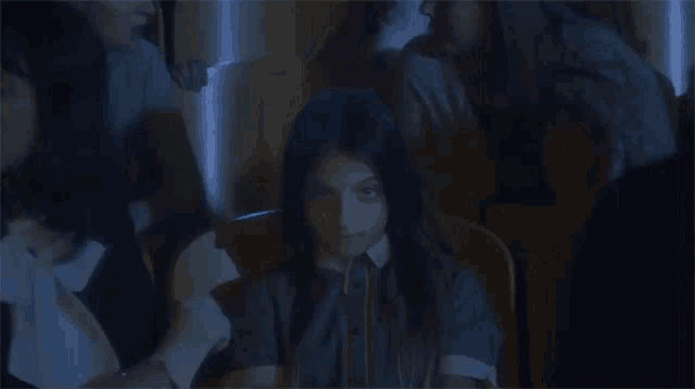 a young girl is sitting in a dark room with a group of people behind her .