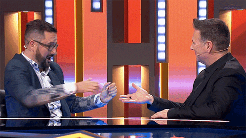 two men are sitting at a table with their hands outstretched