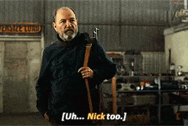 a man with a beard is holding a gun in a garage and talking to someone .