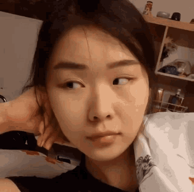 a close up of a woman 's face with her hand on her ear and a shelf in the background .