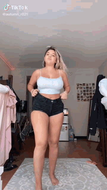 a woman is standing on a rug in a living room wearing shorts and a crop top .