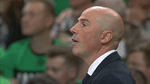 a bald man in a suit and white shirt shouts with his mouth open