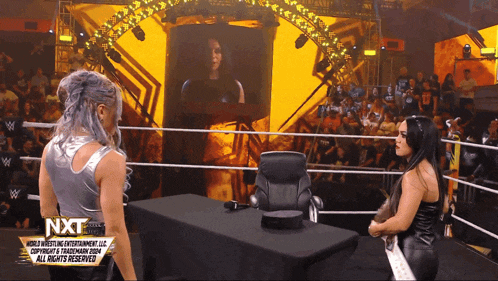 two women standing in a wrestling ring with a sign that says nxt on it