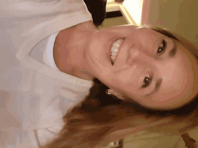 a woman wearing a white shirt and earrings smiles at the camera