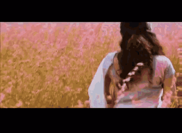 a woman in a white shirt is walking through a field of pink flowers .