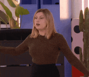 a woman in a brown sweater is standing in front of a cactus