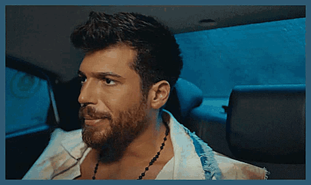 a man with a beard and a necklace is sitting in the back seat of a car .