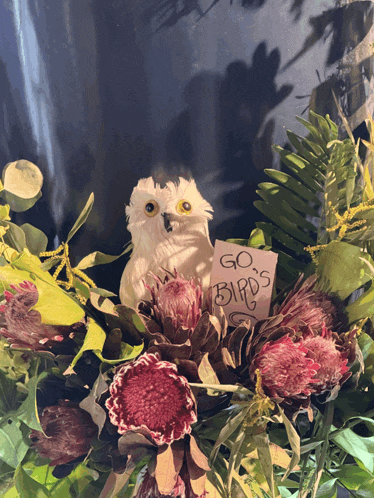 a white owl is sitting in a bouquet of flowers with a card that says go birds