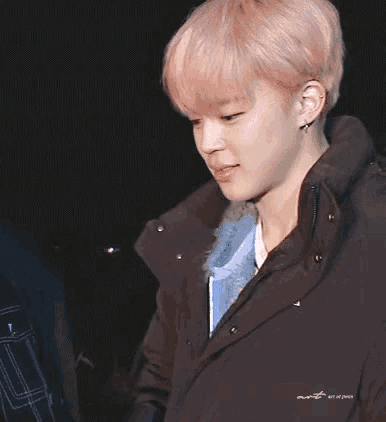 a young man with pink hair is wearing a black jacket and earrings