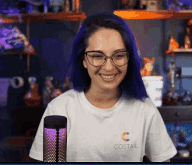 a woman with blue hair and glasses is wearing a white t-shirt that says costail