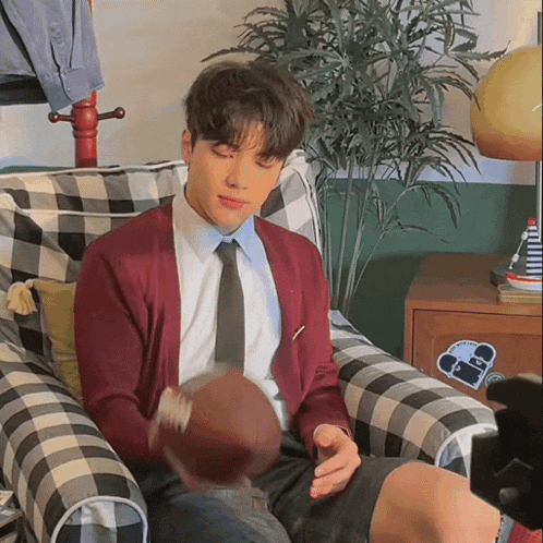 a man in a red cardigan and tie is sitting on a plaid chair holding a football