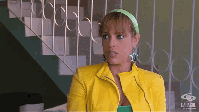a woman in a yellow jacket is standing in front of a staircase with caracol television written on the bottom right
