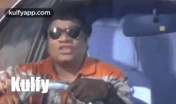a man wearing sunglasses is driving a car while holding a gun .