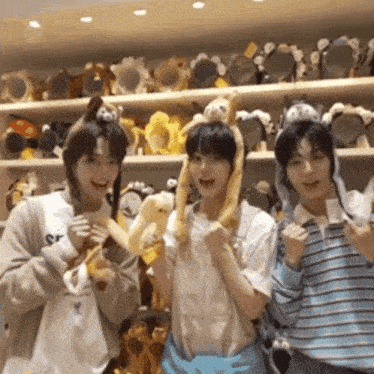 three young men are posing for a picture in front of a shelf full of stuffed animals ..