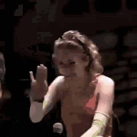a woman in a red tank top and green gloves is waving at a microphone .