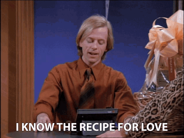 a man in an orange shirt and tie says " i know the recipe for love " while sitting at a table