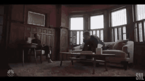 a man is sitting on a couch in a living room with a woman sitting at a table .