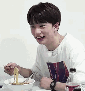 a young man is sitting at a table with a bowl of noodles and a bottle of soda .