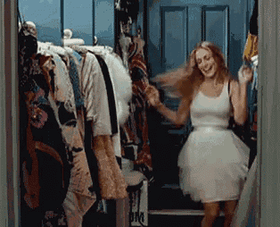 a woman in a white dress is standing in a closet full of clothes .