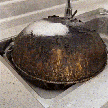 a dirty pot is sitting in a sink with soap coming out of it