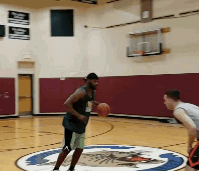 a man dribbles a basketball in a gym with a eagle on the floor