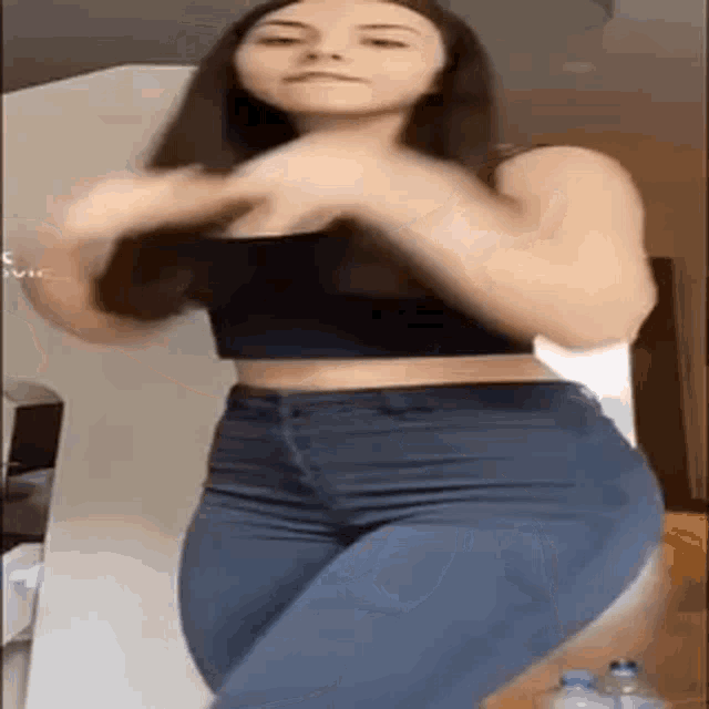 a woman in a black crop top and jeans is dancing in a room .