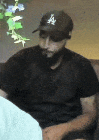 a man with a beard is wearing a black la hat